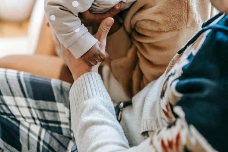 From above of crop anonymous multiracial family interacting with adorable toddler child on blurred background